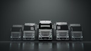 Pięć białych ciężarówek stojących w szarym pomieszczeniu z zapalonymi światłami.