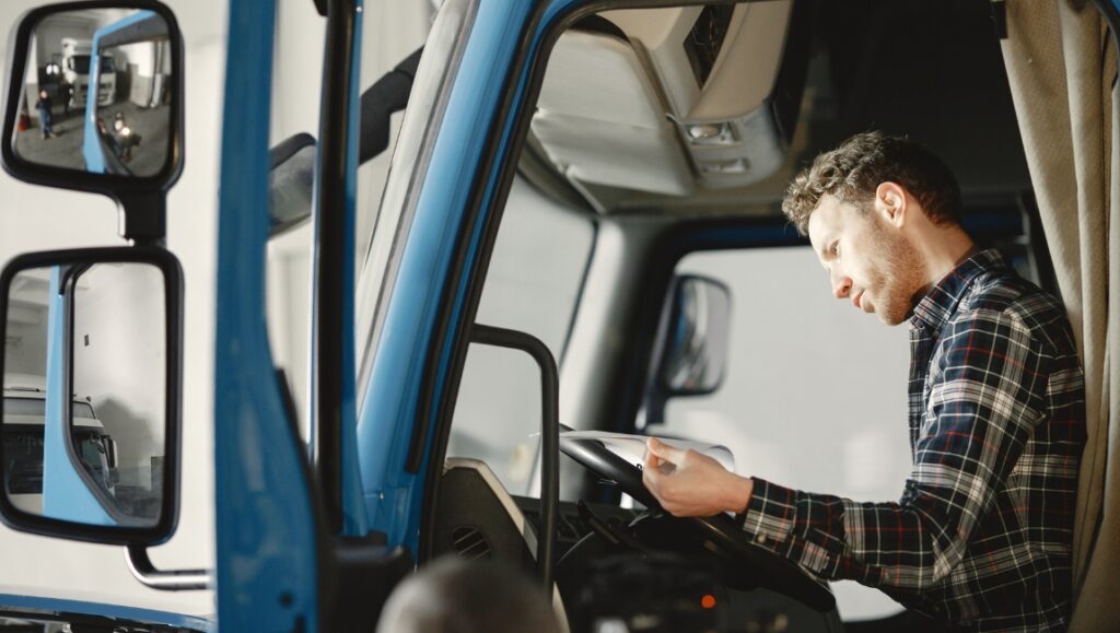 Kierowca ciężarówki siedzi za kierownicą i czyta gazetę.
