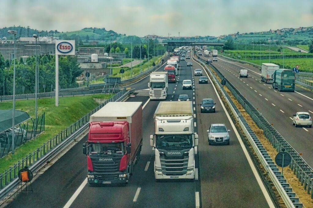 Widok na autostradę czteropasmową a na niej pełno pojazdów. W centrum znajdują się dwie ciężarówki.