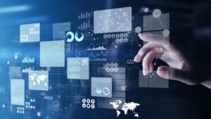 Dłoń sięga w stronę interfejsu złożonego z wielu przezroczystych ekranów zawierających dane, wykresy i ikony związane z analizą informacji.